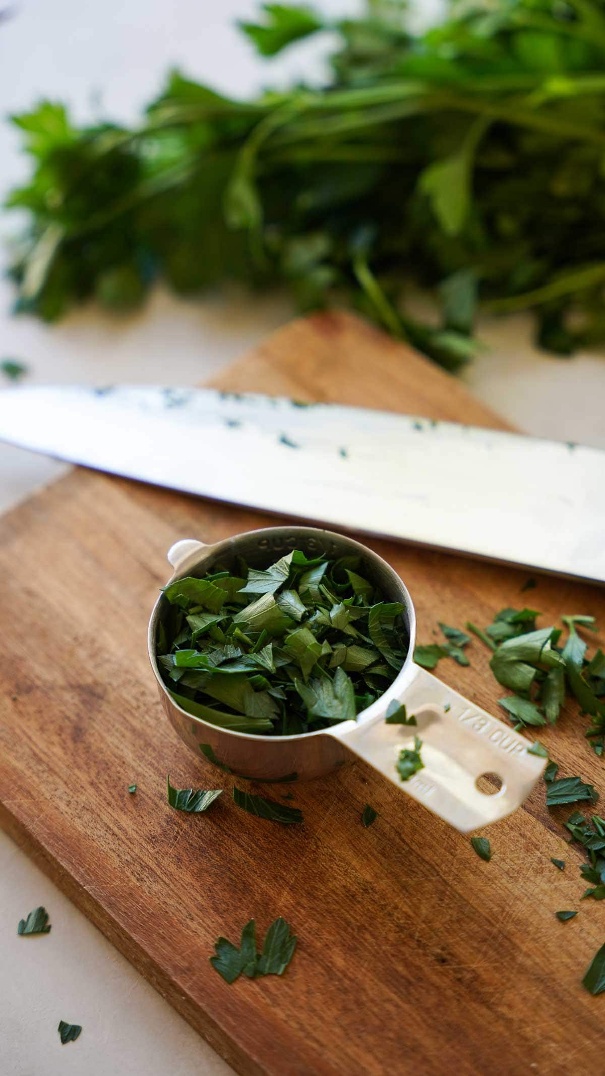 chopped parsley on a board with a quantity measured out in a measuring cup.