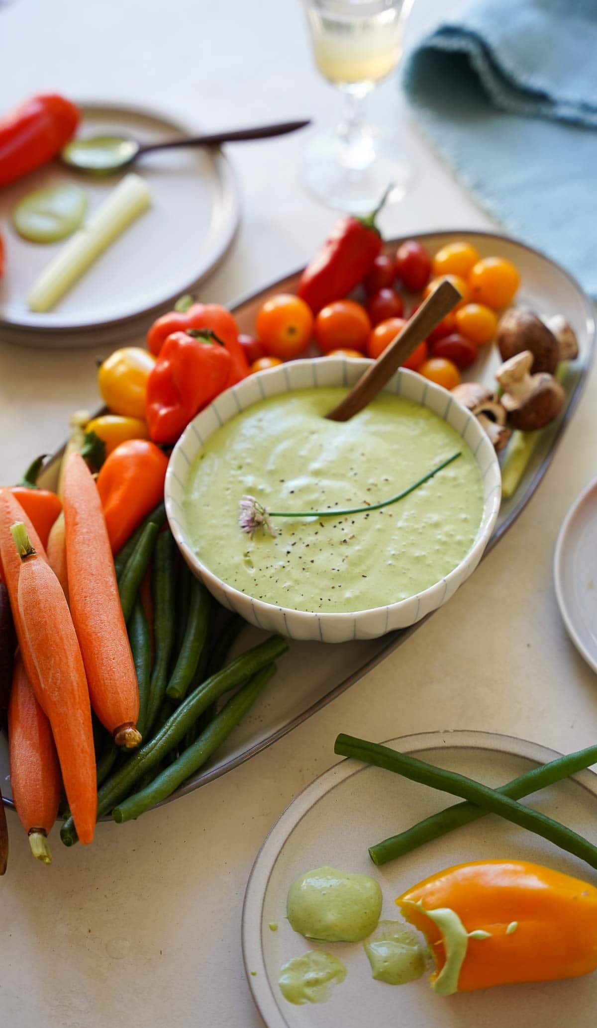 A crudite platter with green goddess dressing in a bowl with vegetables and appetizer plates.