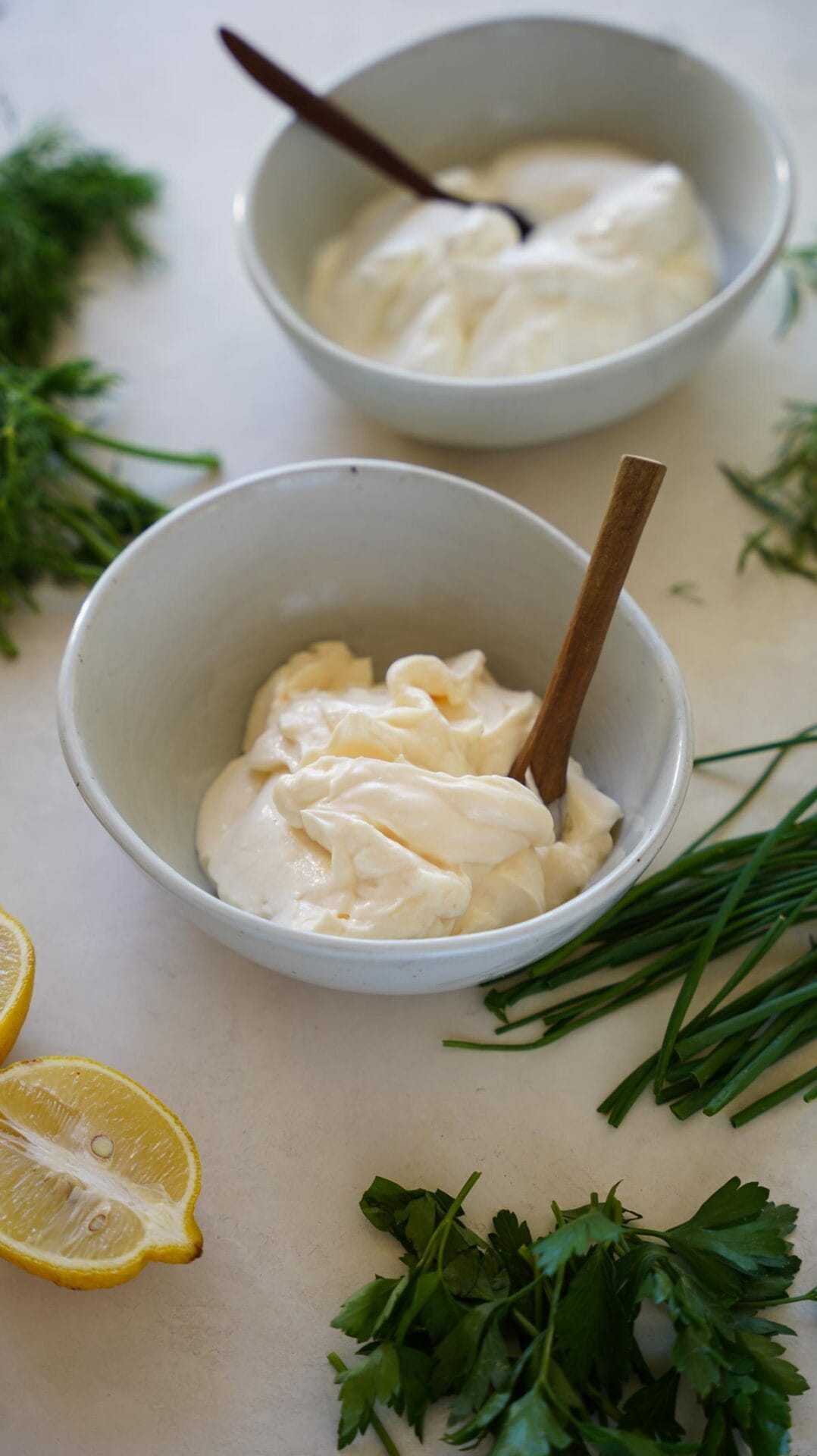 Mayonnaise and sour cream in bowls with fresh herbs and lemon.