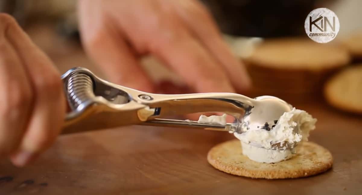 A cookie scoop scooping cheese on a cracker