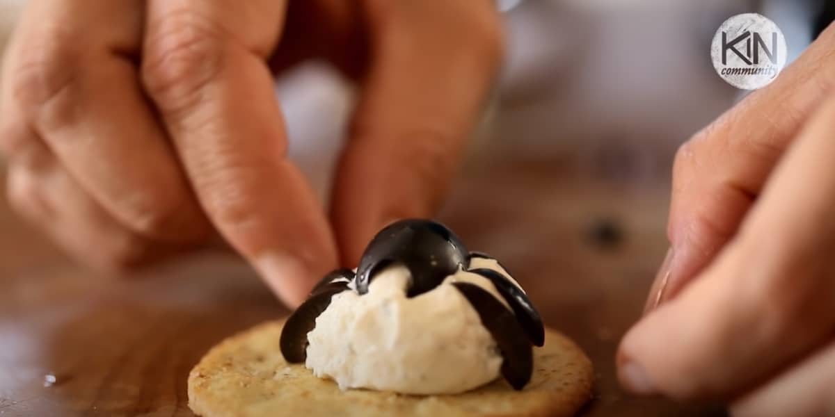 Placing Olive pieces on a cheese mound to resemble a spider