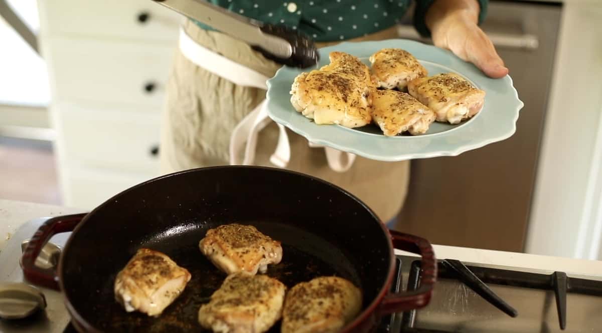 Transferring chicken thighs from a pot to a blue plate with tongs