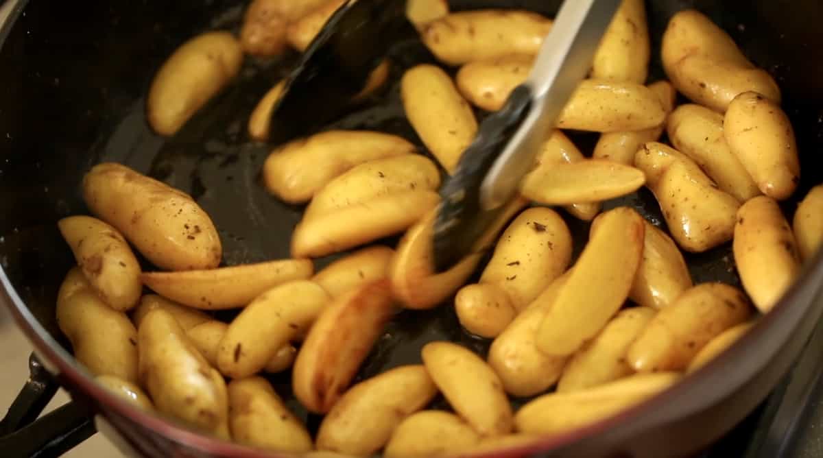 Caramelizing fingerling potatoes in a pot and turning them with tongs