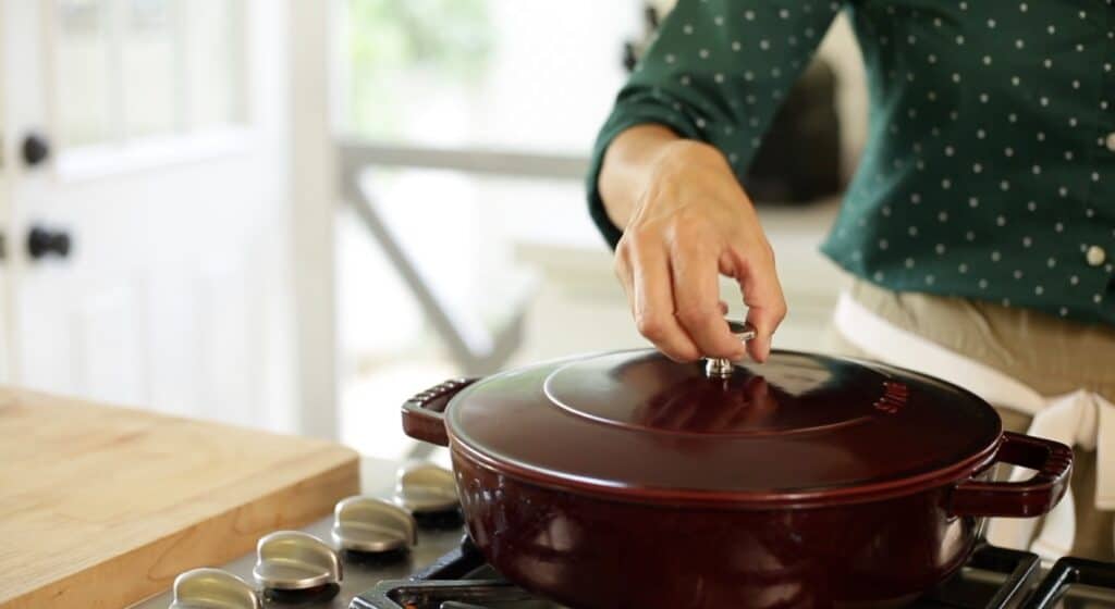 A person placing a lid on a maroon braiser