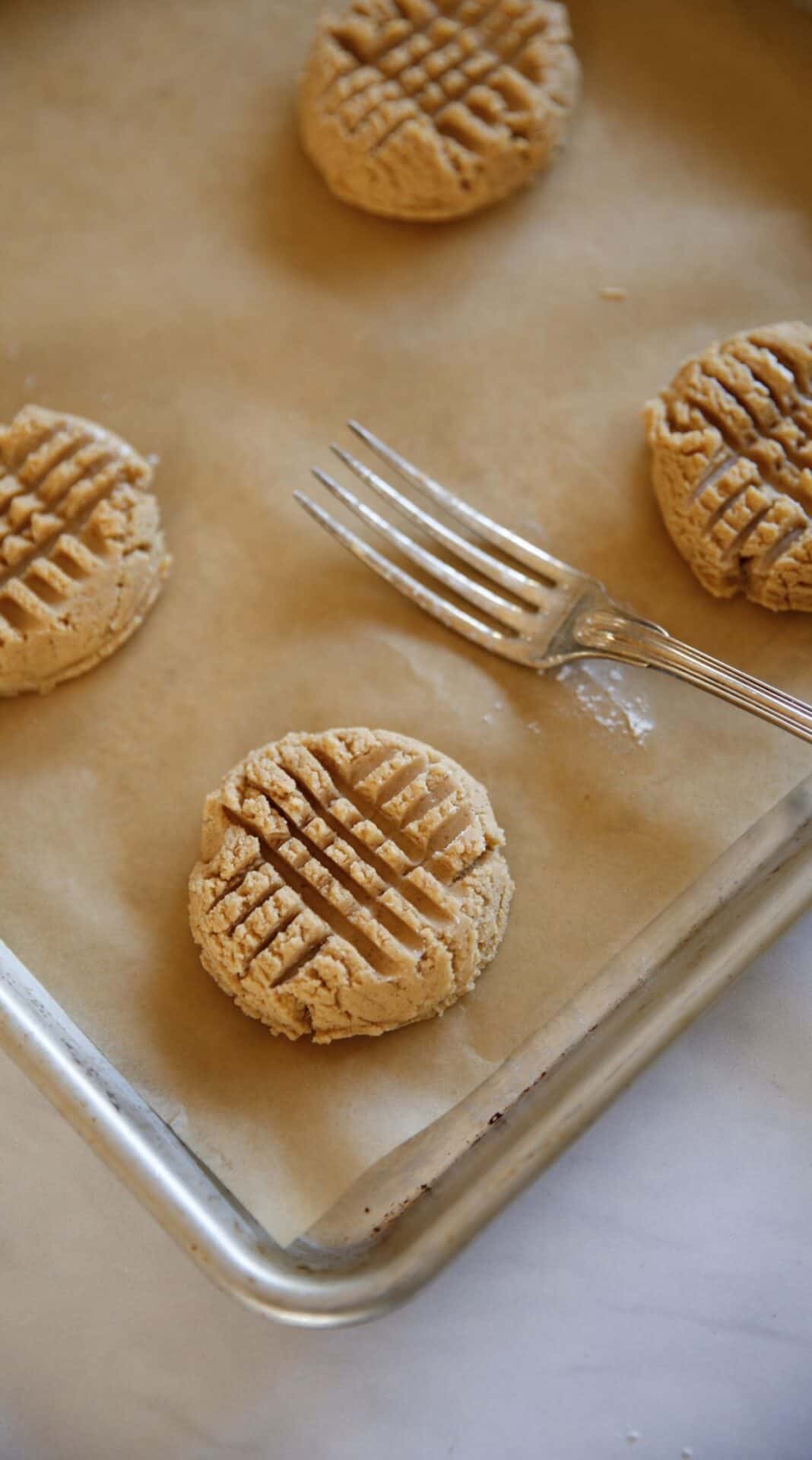 A close up of a fork imprints in a raw peanut butter cookie