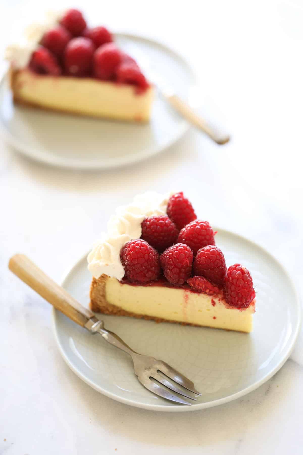 Two slices of cheesecake on plates with fresh raspberries on top
