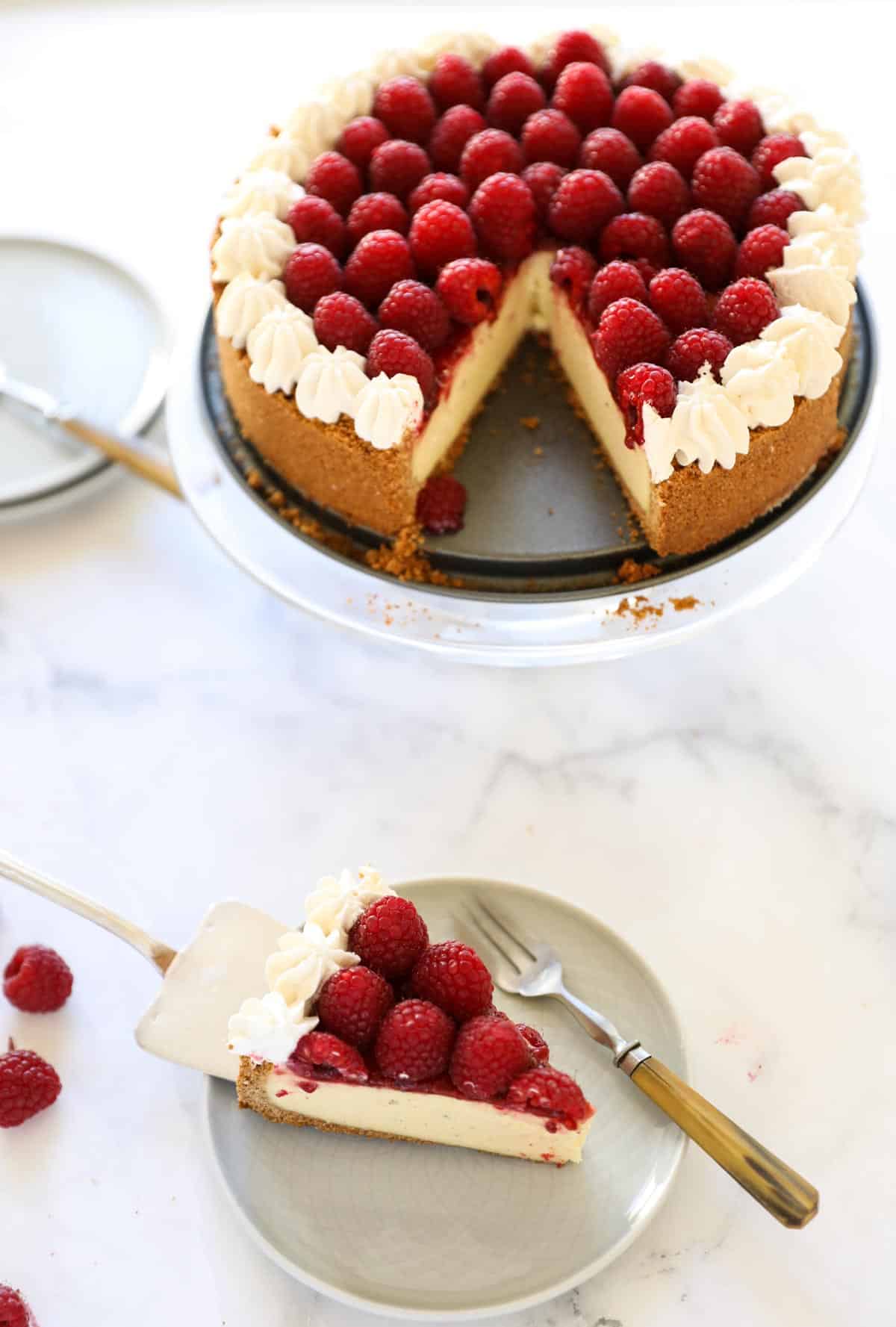A whole raspberry cheesecake with a slice of cake on a plate with a fork