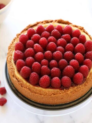 A whole cheesecake decorated with raspberry jam and fresh raspberries