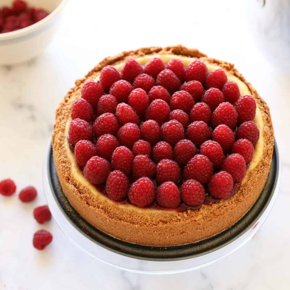 A whole cheesecake decorated with raspberry jam and fresh raspberries