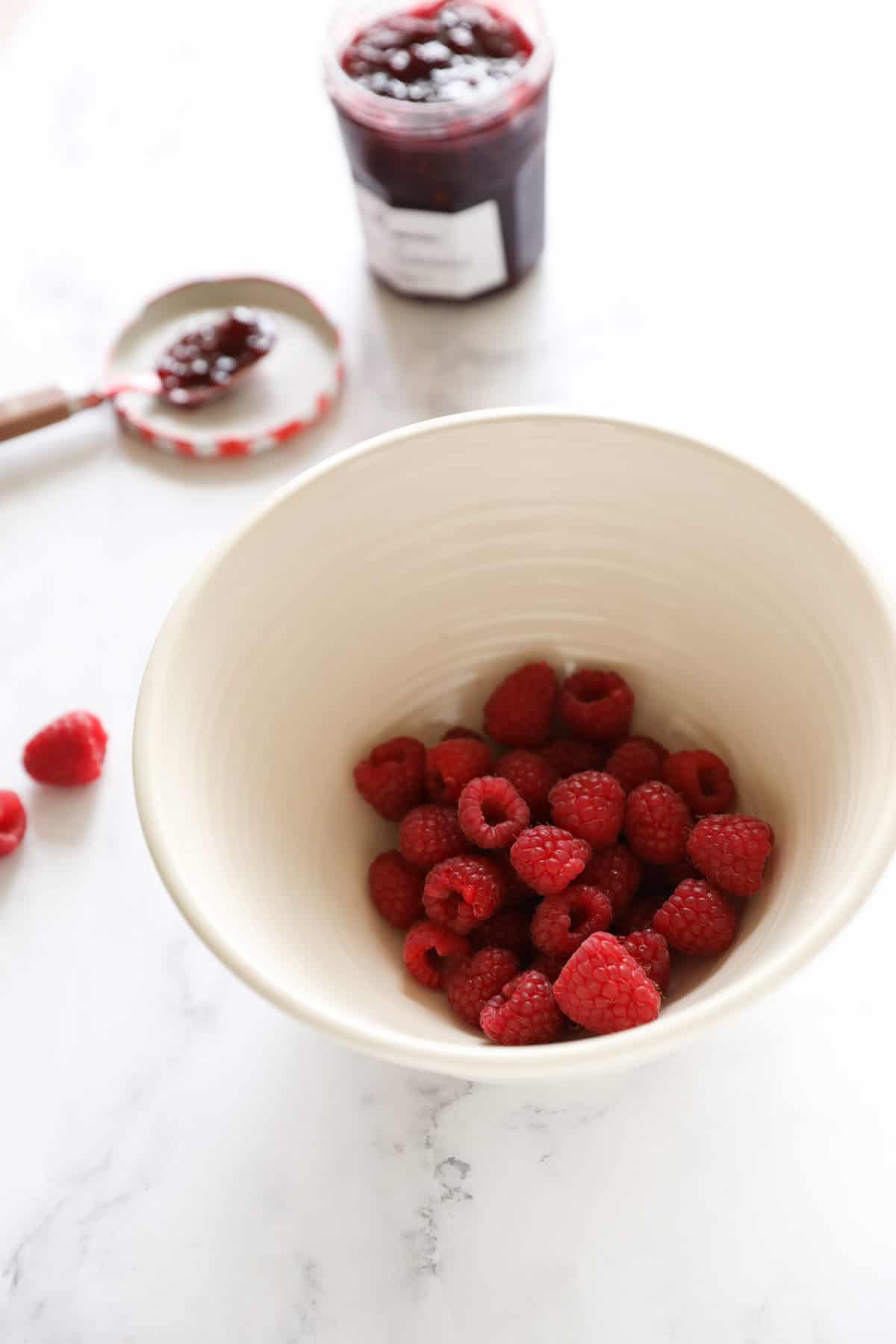 a bowl of fresh raspberries and a pot of raspberry jam in the background