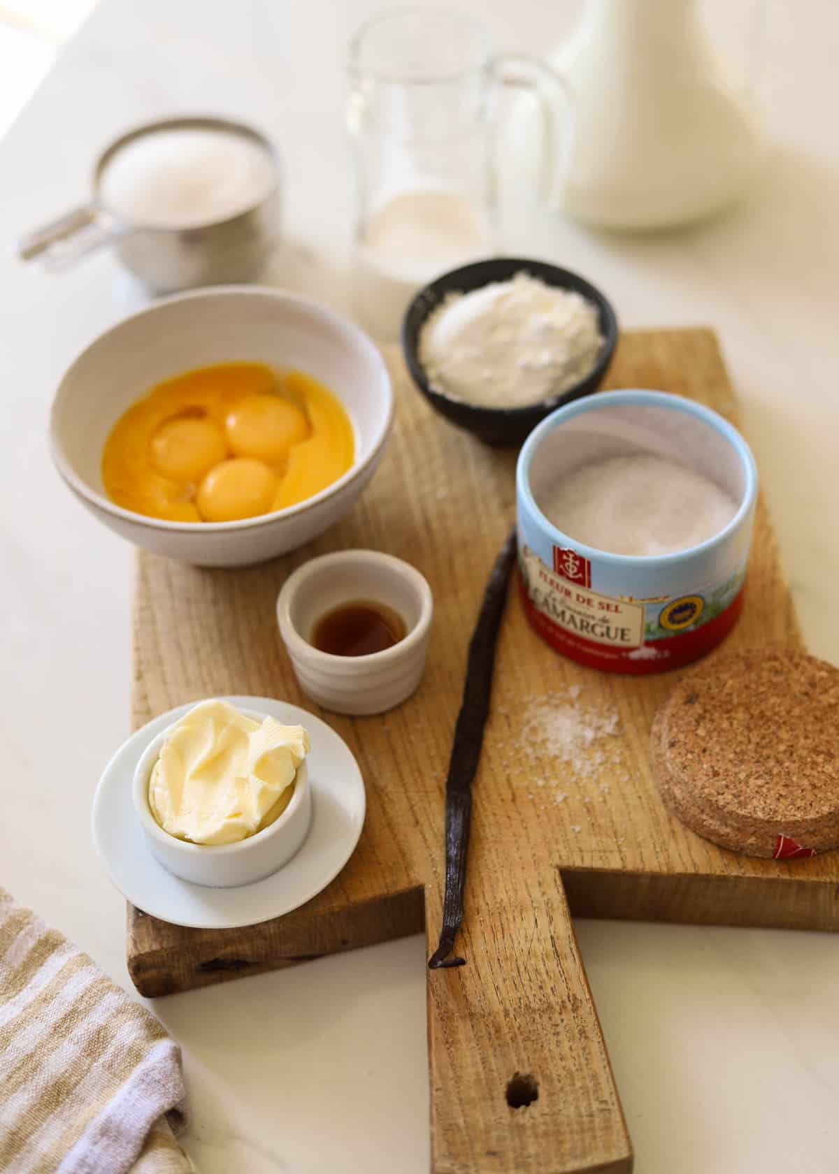 Egg yolks, cornstarch, vanilla bean, vanilla extract and sugar laid on a counter.