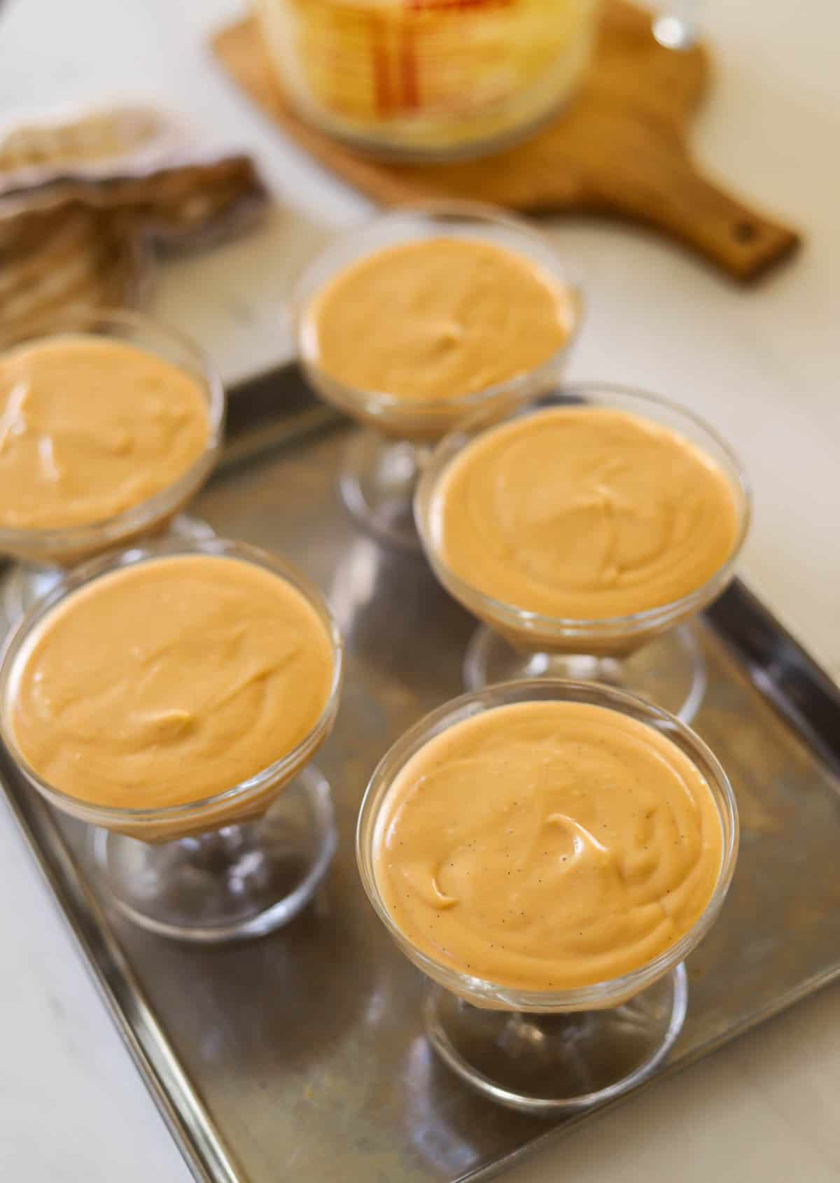 Caramel puddings poured into glass ice cream dishes resting on a tray.