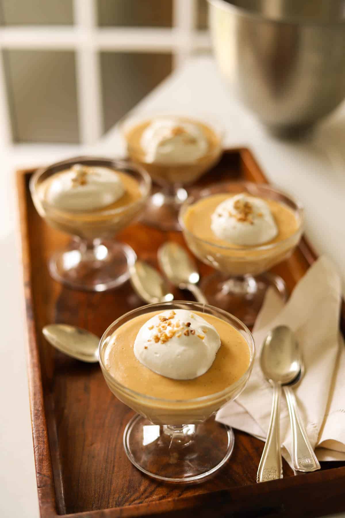 Caramel puddings being topped with a dollop of whipped cream.