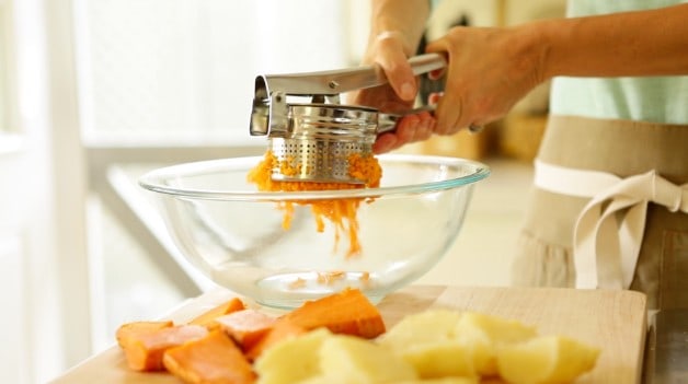 Ricing sweet potatoes into large mixing bowl