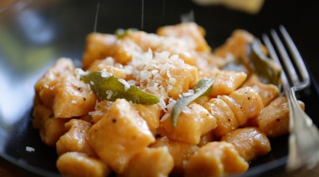 parmesan cheese added to sweet potato Gnocchi with crispy sage leaves in a bowl