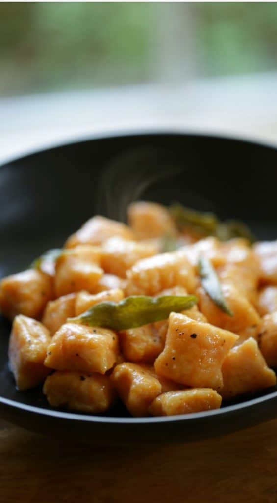 a vertical image of homemade Gnocchi made with sweet potato and topped with Brown Butter and Sage Recipe in a black bowl