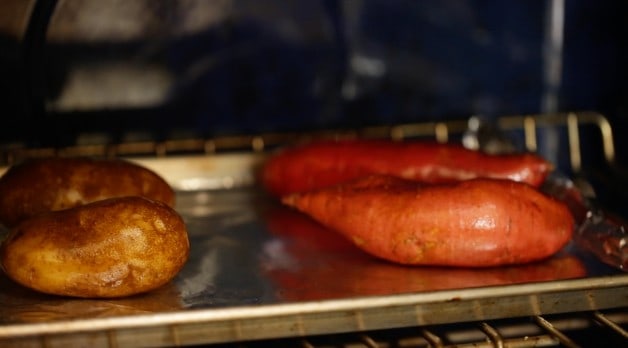 Russet potatoes and sweet potatoes on a sheet pan in the oven 