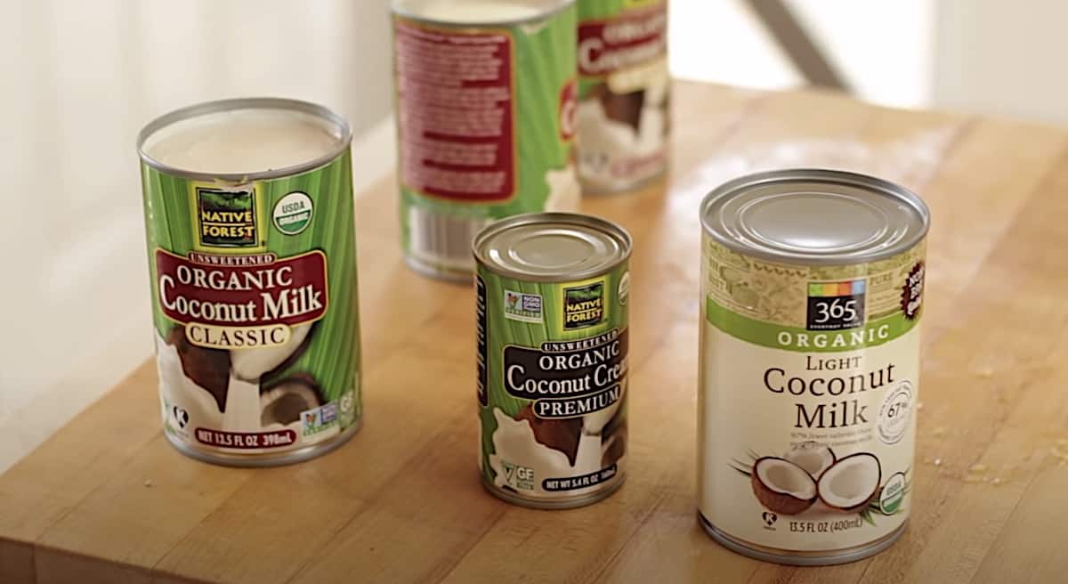 a collection of various styles of coconut milk in cans on a cutting board