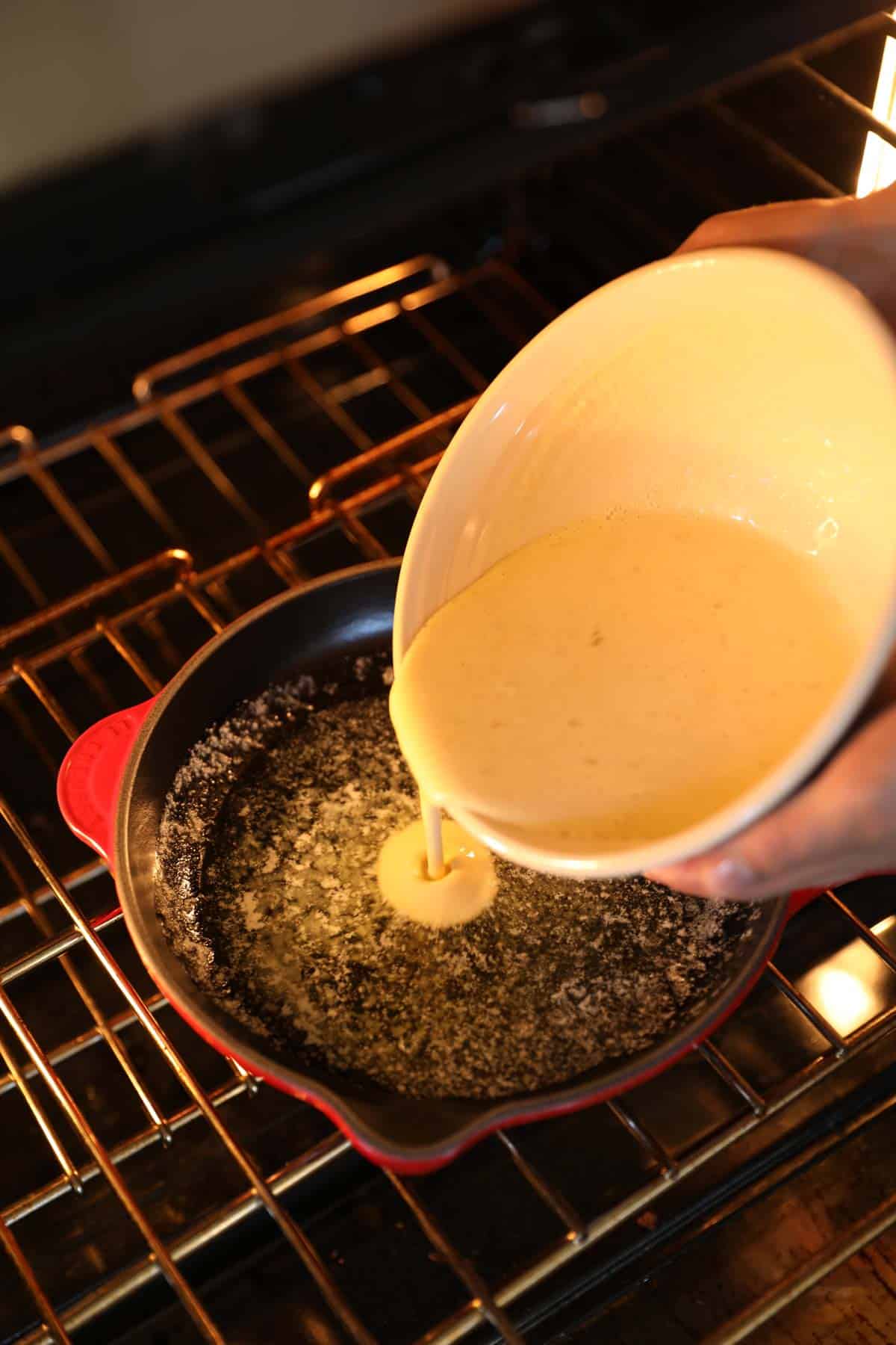 Bowl of pancake batter being poured into a sizzling skillet with butter