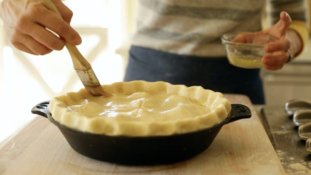 Brushing egg wash onto the top of an apple pie before baking 
