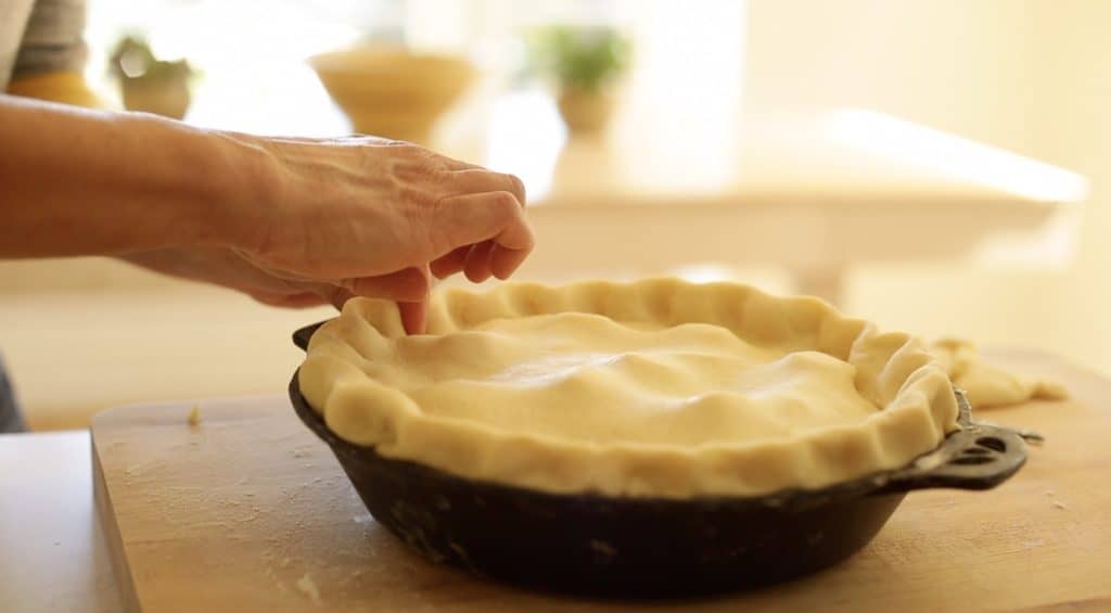 Crimping the edges of pie dough on an apple pie