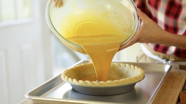 Pouring pumpkin pie filling into pin shell resting on a baking sheet