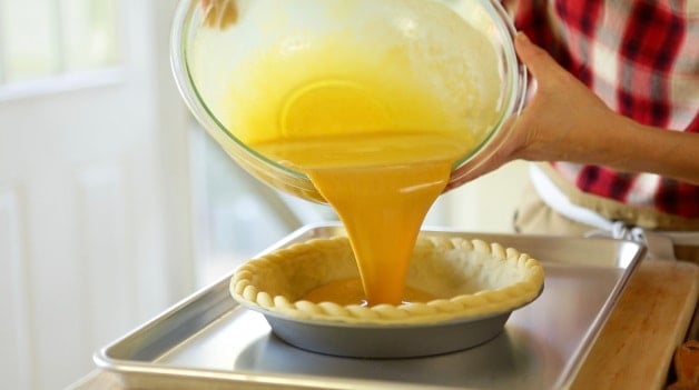 Pouring pumpkin pie filling into pin shell resting on a baking sheet