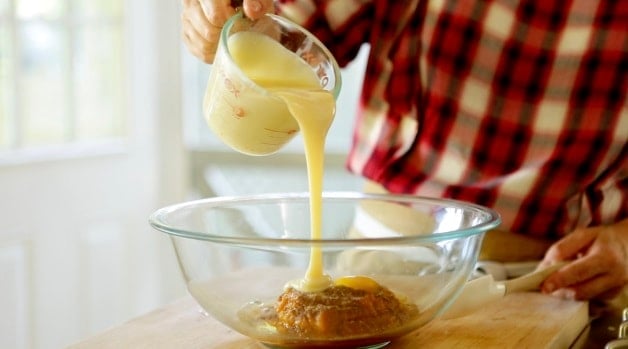 Pouring Sweetened condensed milk into bowl with pumpkin puree