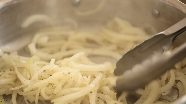 Onions in pan cooking while metal tongs stir them