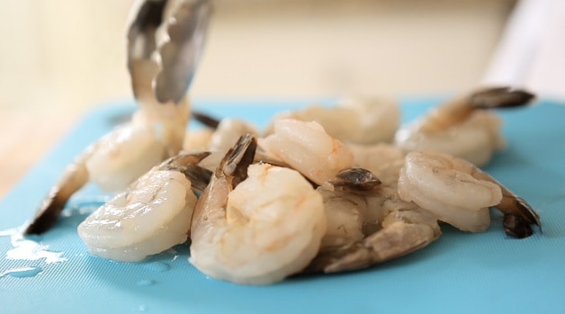 Raw shrimp on a blue cutting board mat