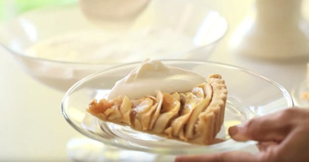 Slice of a French Apple Tart with whipped cream on a glass plate