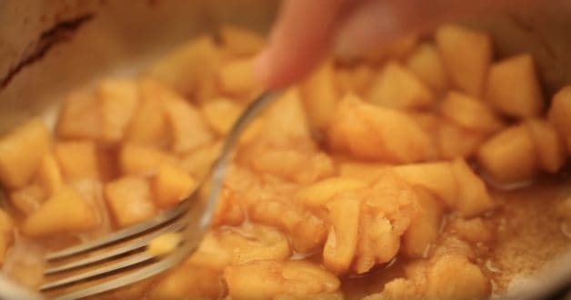 Fork pressing down apples in a pot to make compote