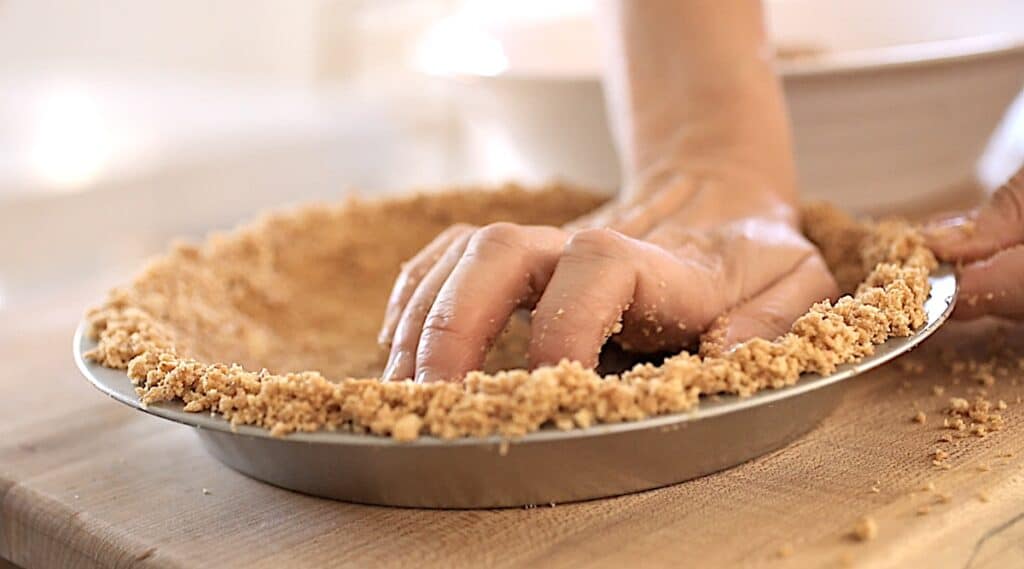 a hand forming a graham cracker crumb in a pie plate