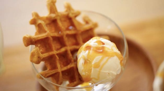 a glass ice cream dish filled with ice cream, topped with caramel sauce and served with a pumpkin waffle on the side