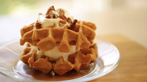 a pumpkin waffle ice cream sandwich topped with whipped cream and chopped pecans