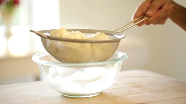Lifting a fine mesh sieve filled with ricotta cheese over a glass bowl 