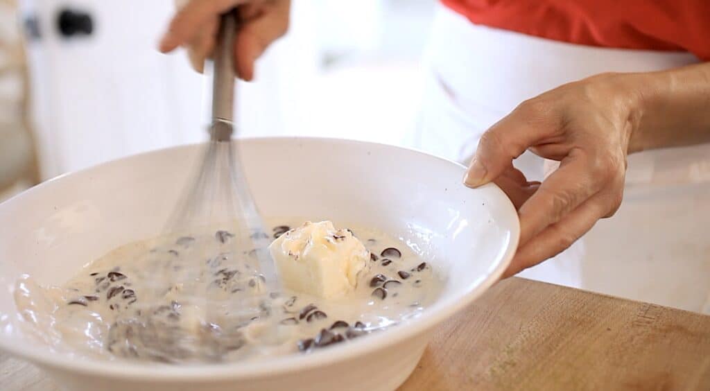 a person whisking hot cream mixture with chocolate chips and butter