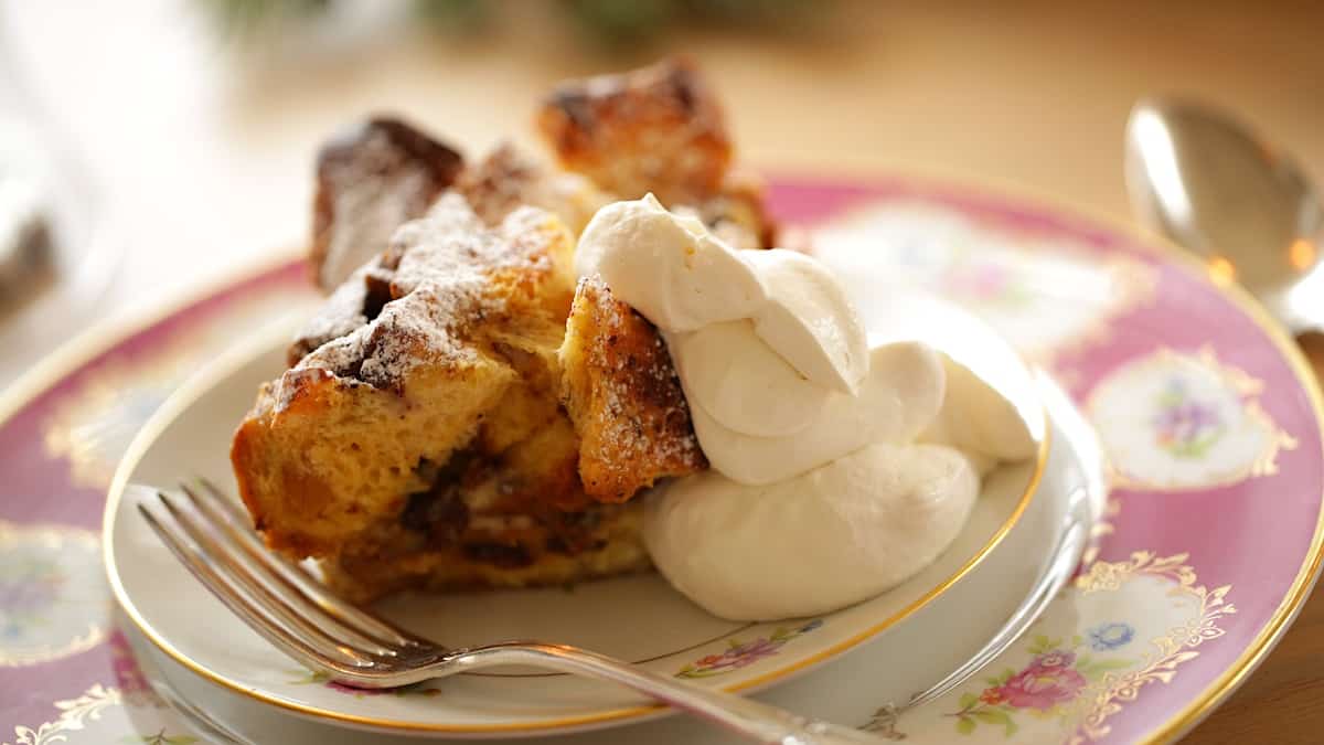 a serving of breadpudding on an aniqure plate with a fork and softly whipped cream