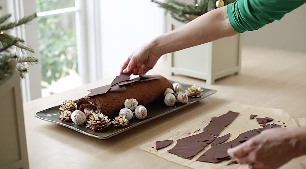 a person placcing chocolate bark on top of yule log