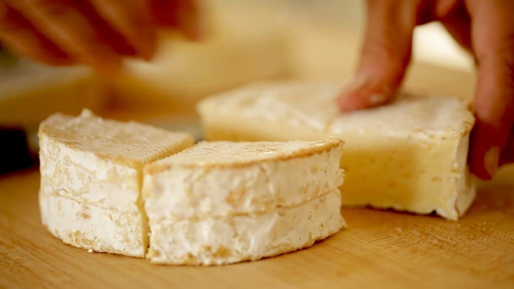 slicing a wheel of cheese into quarters