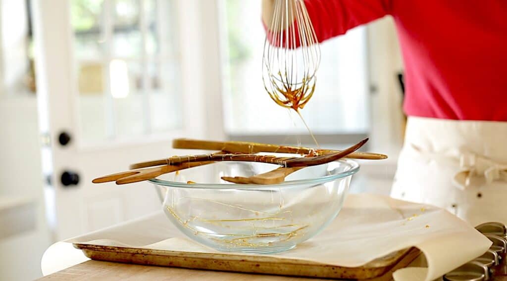 a person moving a whisk dipped in hot caramel across wooden spoons