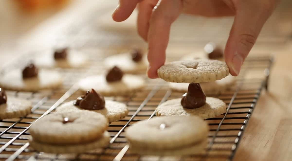 a person adding linzer cookie tops to a cookie bottom with Nutella in the center