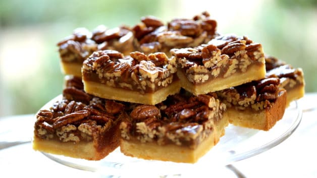 Pile of sliced pecan bars sliced into rectangles on a glass cake stand