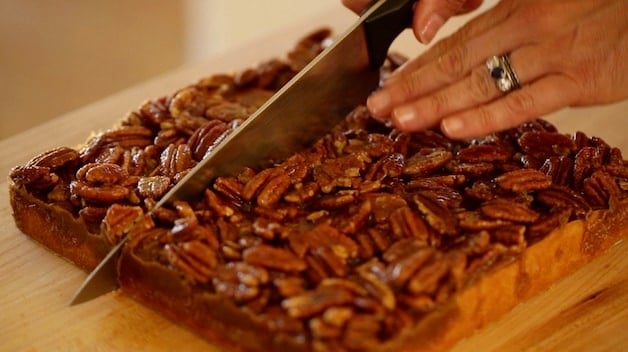 Slicing freshly baked pecan bars on a cutting board