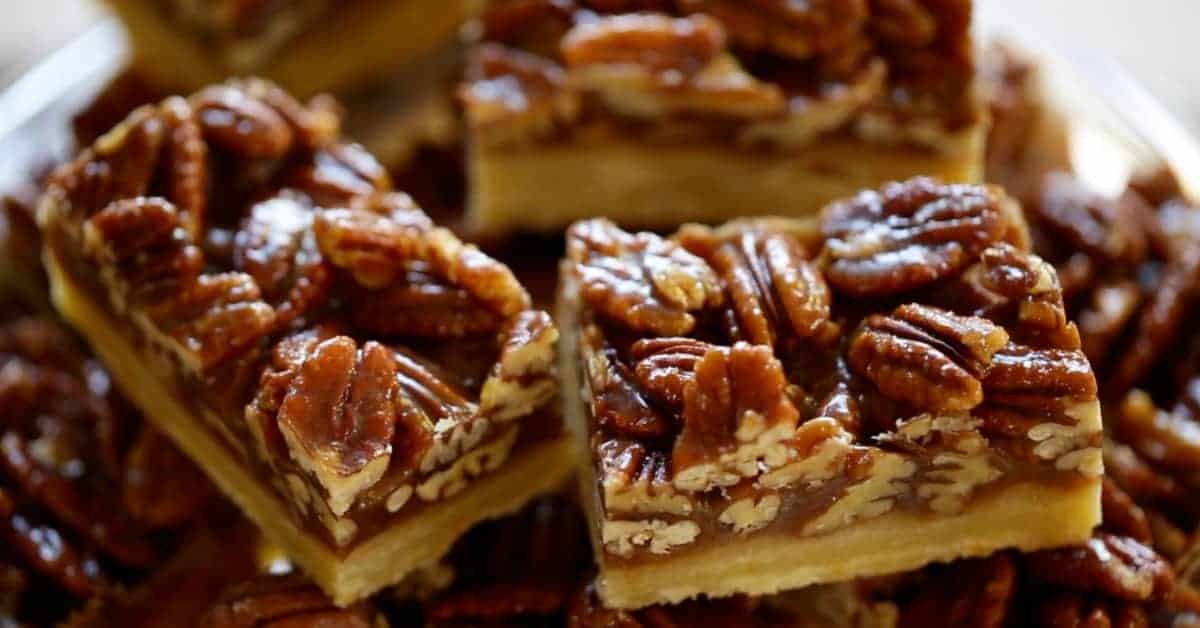 Sliced pecan bars piled on a glass cake stand