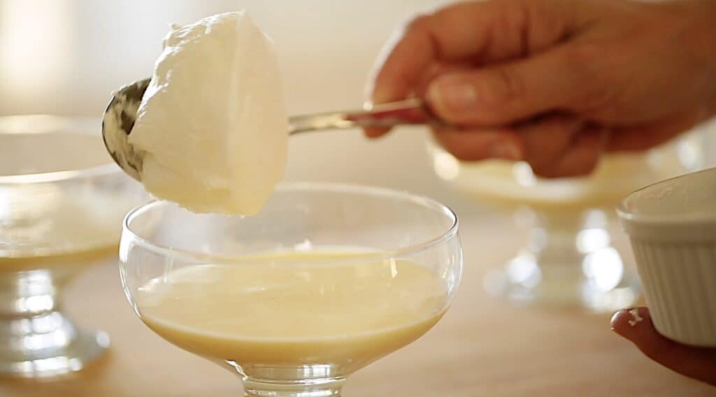 adding a scoop of baked meringue on top of creme anglaise in a clear bowl