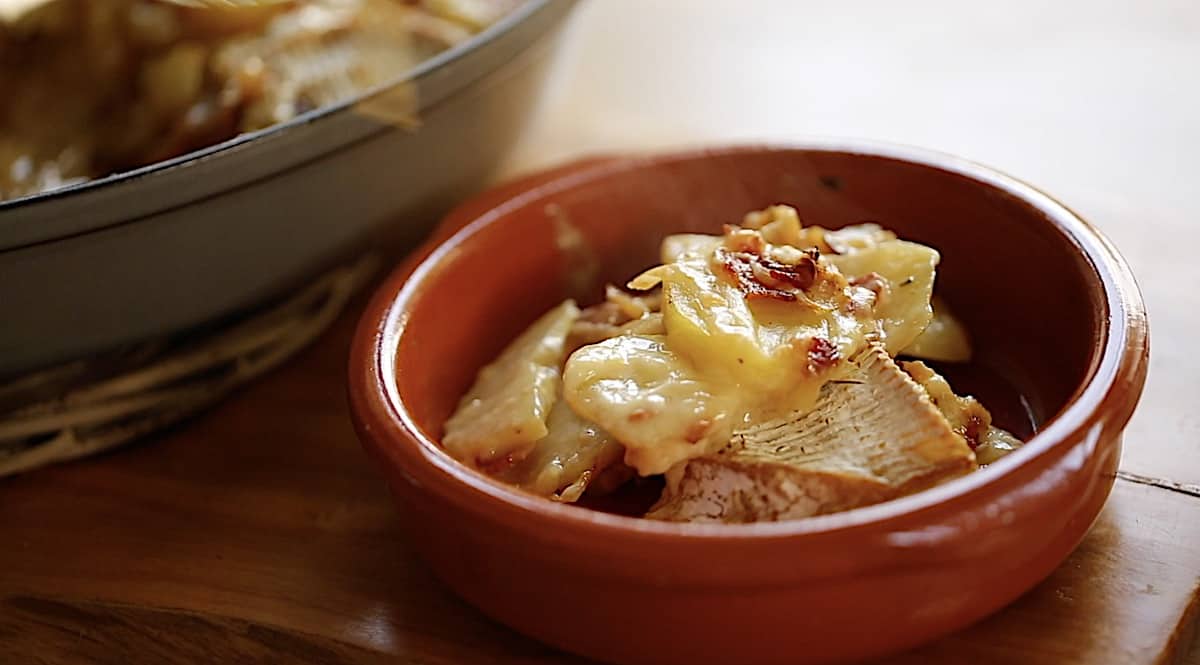 a serving of potatoes, bacon and brie in terra cotta bowl