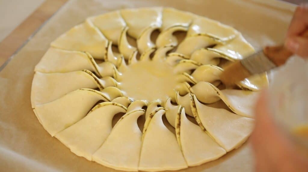 brushing egg wash on to a tarte au soleil before baking it