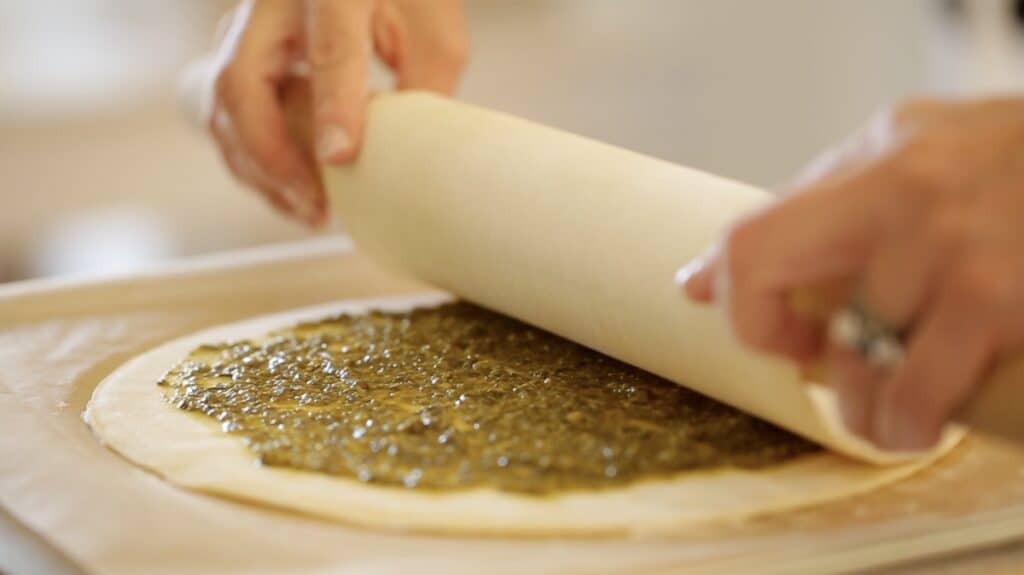 adding a second puff pastry round to an existing round filled with pesto sauce