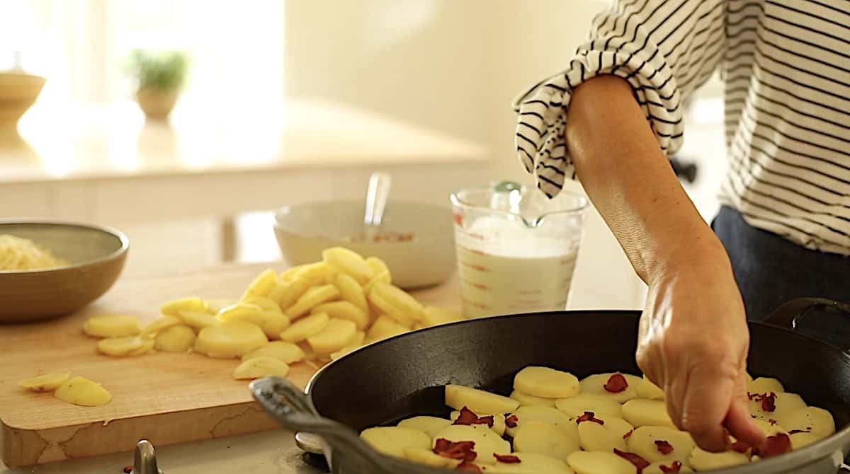 layering potatoes and bacon in a gratin dish